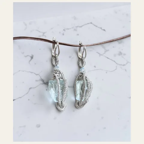 Aros Fragmentos de Iceberg: aros colgantes de encaje frivolité tejido a mano en hilo metalizado plateado, con cristal en bruto celeste de aspecto mineral y cuenta facetada celeste