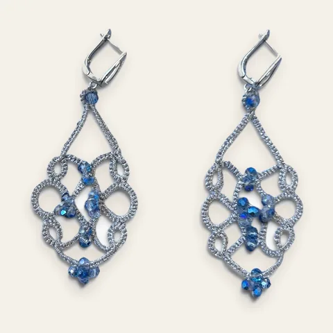 Aros Mañana Helada: aros largos de encaje frivolité tejido a mano en hilo metalizado plateado, con cristal facetado azul con reflejo tornasolado