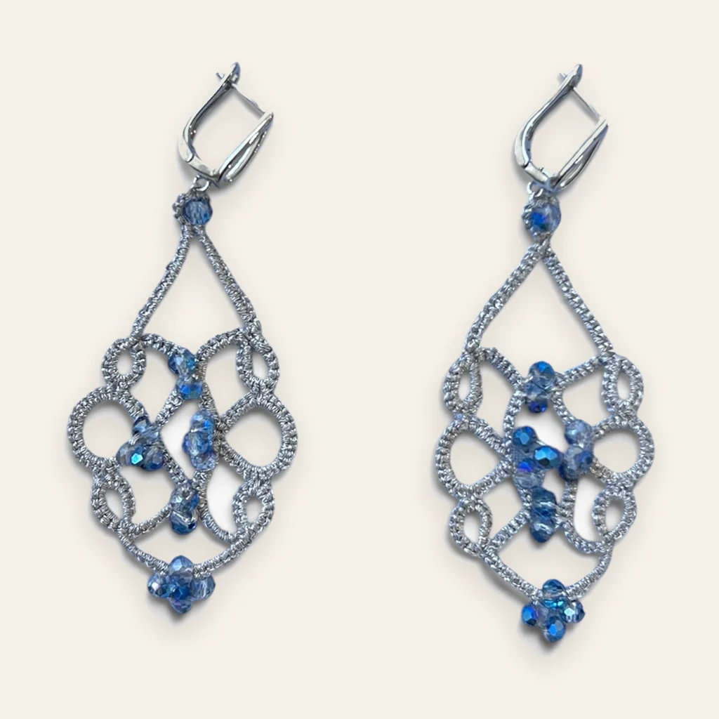 Aros Mañana Helada: aros largos de encaje frivolité tejido a mano en hilo metalizado plateado, con cristal facetado azul con reflejo tornasolado