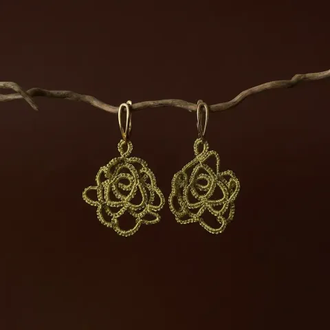 Aros Rosa Dorada de encaje frivolité con forma de rosa dorada, colgados de una rama sobre fondo marrón oscuro