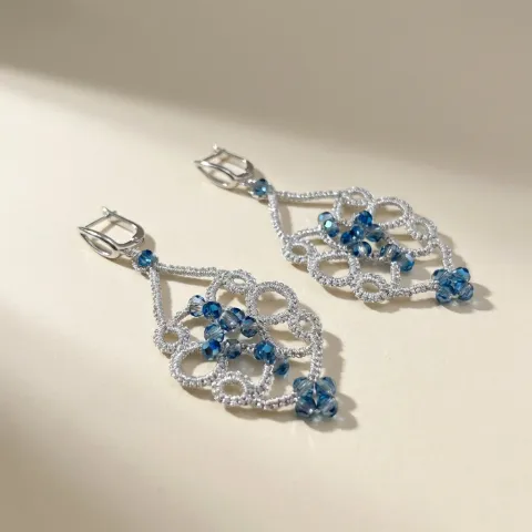 Aros Vals Azul de encaje frivolité plateado con cristales azules, sobre fondo beige claro