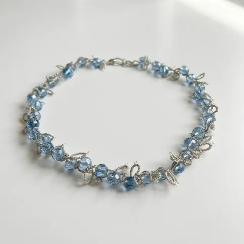 Collar Cristal Azul de encaje frivolité con cuentas facetadas celestes e hilo plateado, sobre fondo blanco