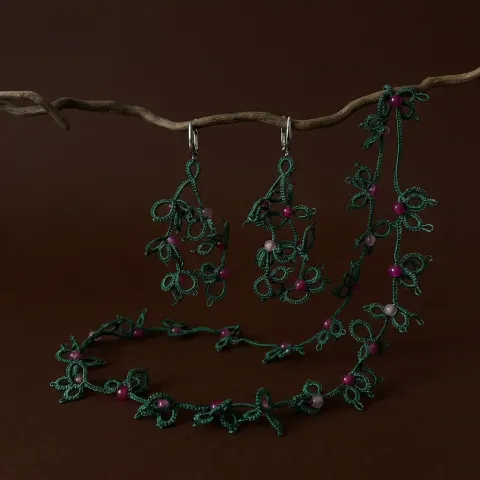 Conjunto Enredadera Esmeralda de encaje frivolité verde con mostacillas fucsias, colgado de una rama sobre fondo marrón